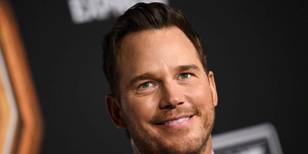 Chris Pratt smiles and looks upward in a bright lilac shirt and suit on the red carpet